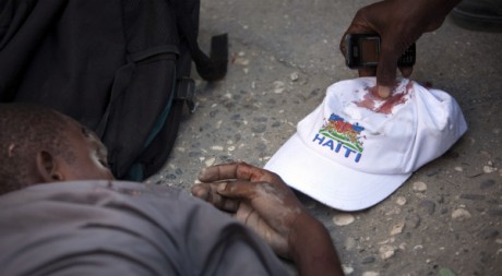 Un homme ramasse la casquette d'Ivarol Louis, le jeune homme à terre, à Port-au-Prince, le 25 nov 2010. REUTERS/Allison Shelley